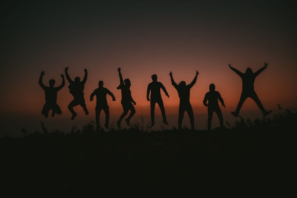 Silhouetten van een groep mensen die samen opspringen bij zonsondergang
